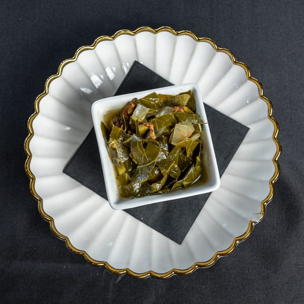 Southern Fresh collard greens with onions and meat in a white bowl on a decorative plate.