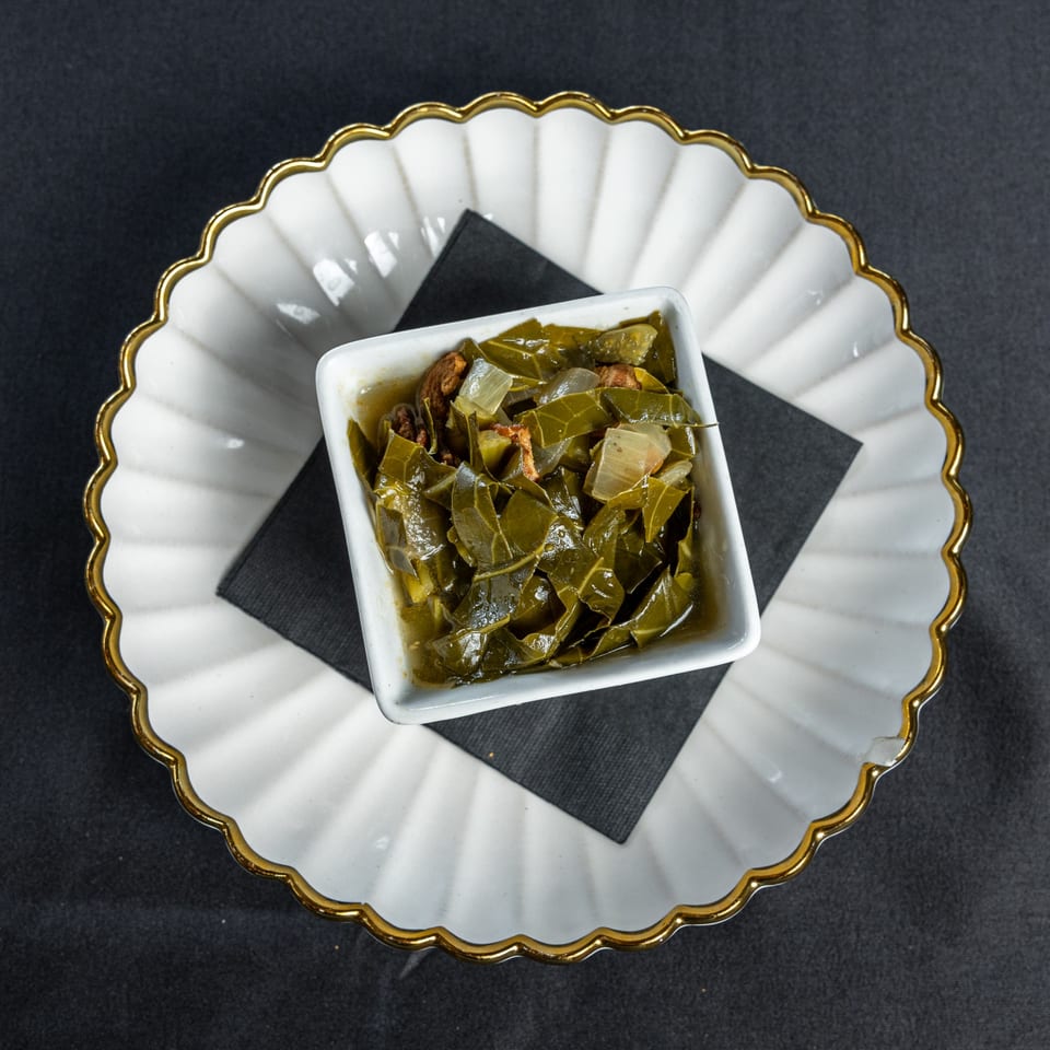 Southern Fresh collard greens with onions and meat in a white bowl on a decorative plate.