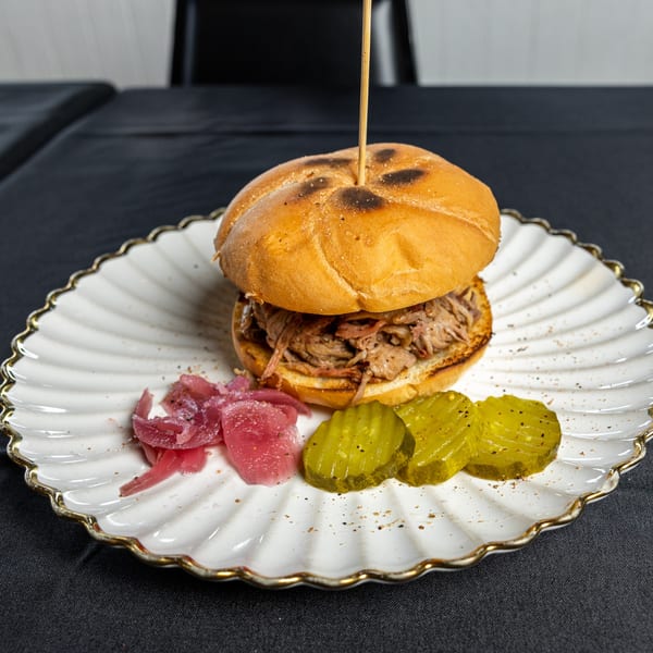 Southern Fresh pulled pork sandwich with pickled onions and pickles on a white scalloped plate.