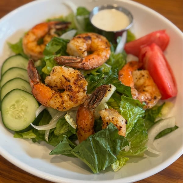A Southern Fresh grilled shrimp salad with lettuce, cucumbers, tomatoes, onions, and dressing.